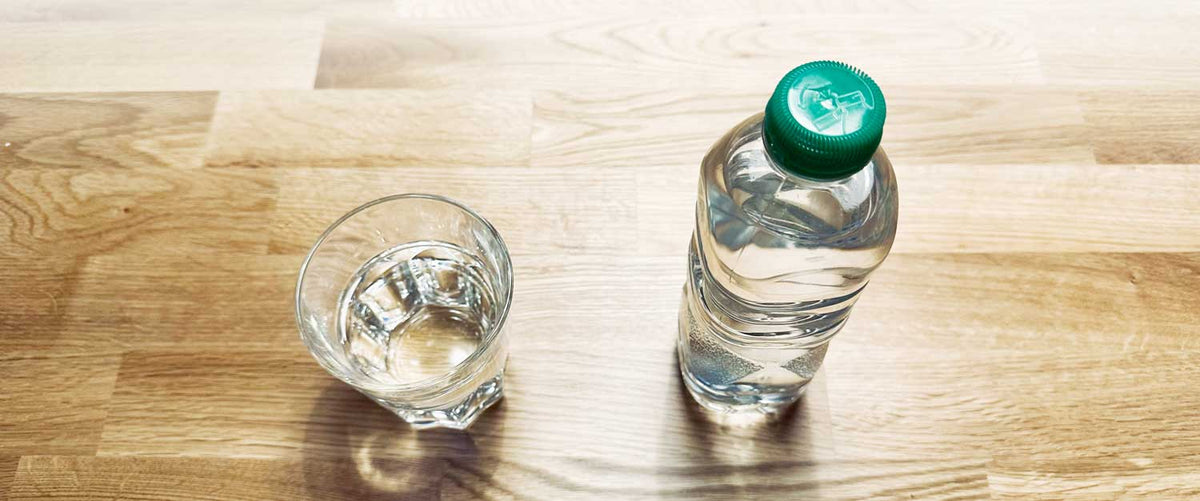 Wasserflasche neben einem gefüllten Glas Wasser als Symbolbild für den Vergleich von Mineralwasser und Leitungswasser.