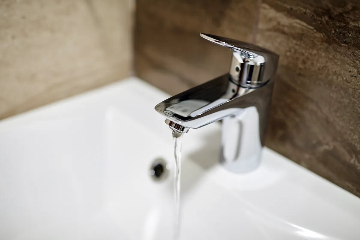 Moderner Wasserhahn mit fließendem Wasser im Bad