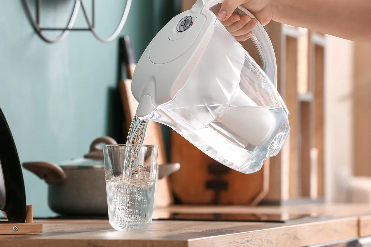 Frau gießt Wasser aus einem Tischkannenfilter ins Glas